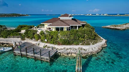 Fowl Cay Private Island Resort, Bahamas, Fly Unique, Privatinsel, Inselresort, Bootsanleger, Tropeninsel, Karibik, Luxusreise, Luftaufnahme Das Foto zeigt das Fowl Cay Private Island Resort auf den Bahamas. Eine einzelne Villa steht auf einer kleinen Privatinsel mit dichtem Grün, privatem Bootsanleger und kristallklarem, türkisfarbenem Wasser; die Aufnahme ist eine schräge Luftansicht mit Blick auf die umliegenden Lagunen.