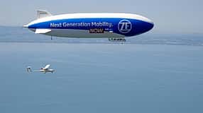 Technoflug Piccolo und Zeppelin NT in der Luft über einem See, vermutlich Bodensee, aus der Luft fotografiert. Das Luftschiff trägt die Aufschrift 'Next Generation Mobility. ZF NOW.' und ein einmotoriges Leichtflugzeug (Technoflug Piccolo) fliegt darunter.