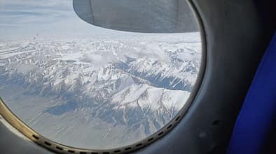 Blick aus einem Flugzeugfenster auf schneebedeckte Berge und Wolken.