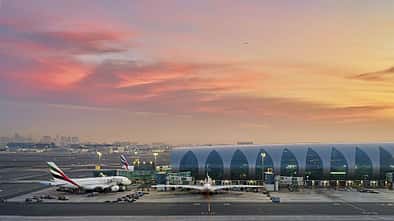 Flughafen mit geparkten Emirates-Flugzeugen vor einem modernen Terminalgebäude bei Sonnenuntergang.