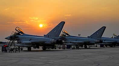 Das Foto zeigt mehrere Eurofighter Typhoon der Luftwaffe während der Übung Pitch Black. Die Kampfflugzeuge stehen mit geöffneten Cockpithauben auf dem Vorfeld, umgeben von Leitern und Bodenunterstützungsgeräten; die Eisernen‑Kreuz‑Kennzeichen und deutsche Flaggen an den Seitenleitwerken sind sichtbar. Die tief stehende Sonne erzeugt Silhouetten vor einem orangefarbenen Himmel.