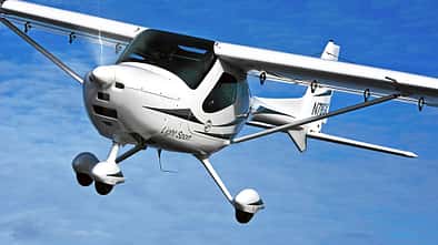 Das Foto zeigt ein Remos GX Leichtsportflugzeug (Light Sport Aircraft) im Flug. Der Hochdecker in Verbundbauweise besitzt ein Bugradfahrwerk und wird laut IPTC von einem 100‑hp Rotax 912 angetrieben. Die Aufnahme zeigt die Maschine über dem Beaver Lake bei Rogers, Arkansas (USA).