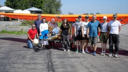 Gruppenfoto von Jugendlichen und Erwachsenen vor einem orangefarbenen Ultraleichtflugzeug nach dem Erstflug im Rahmen eines OUV-Jugendprojekts.