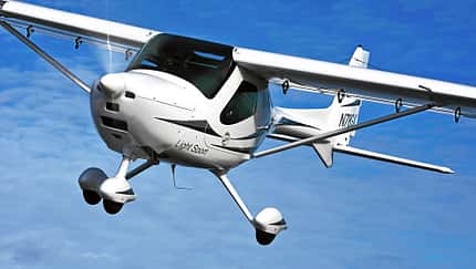 Das Foto zeigt ein Remos GX Leichtsportflugzeug (Light Sport Aircraft) im Flug. Der Hochdecker in Verbundbauweise besitzt ein Bugradfahrwerk und wird laut IPTC von einem 100‑hp Rotax 912 angetrieben. Die Aufnahme zeigt die Maschine über dem Beaver Lake bei Rogers, Arkansas (USA).