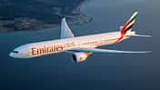 Boeing 777-300ER von Emirates bei einem Flug im Sonnenuntergang über Wasser